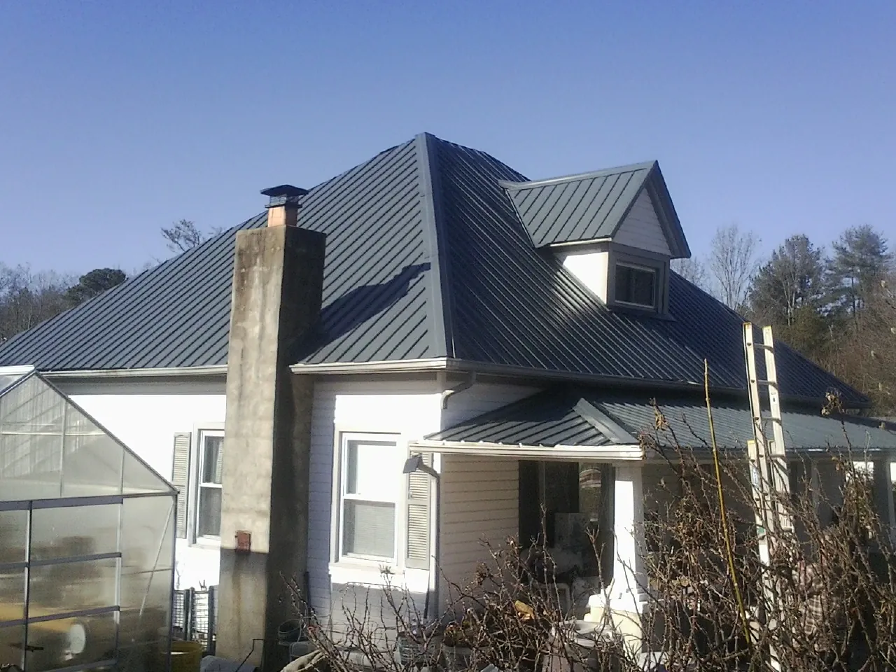 Dark blue standing seam metal roof on a white farmhouse with dormer — Slate & Tile Roof Repair by Roofing Brothers in Sterling Heights