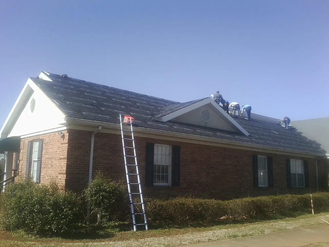 Crew tearing shingles off a brick ranch roof with a ladder set — Metal Roof Repair work by our crew in Sterling Heights