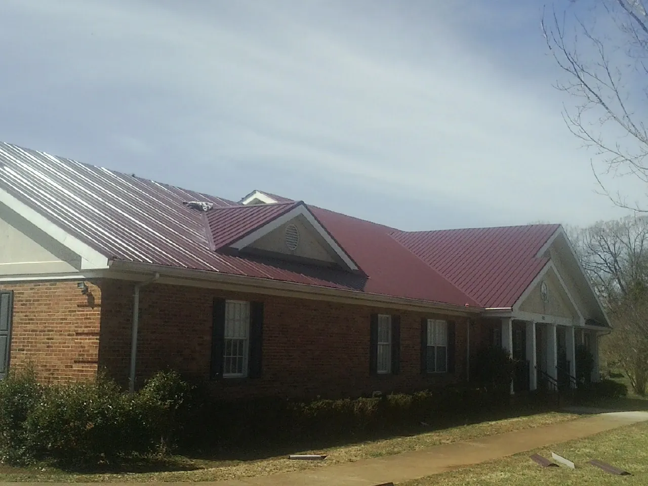 Red metal roof with gabled entries on a long brick building, from a Hail Damage Roof Repair job in Sterling Heights