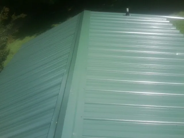 New green metal panels meeting at the ridge of a roof — Flat Roof Repair work by our crew in Sterling Heights