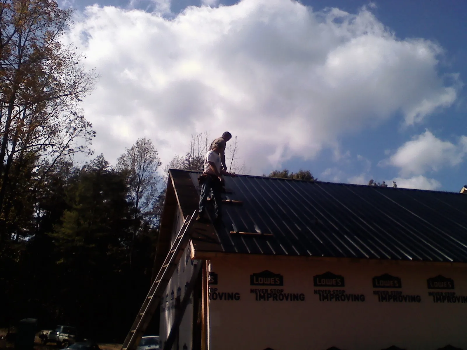 Roofer fastening dark metal panels high against a cloudy sky, from a Roof Inspection job in Sterling Heights