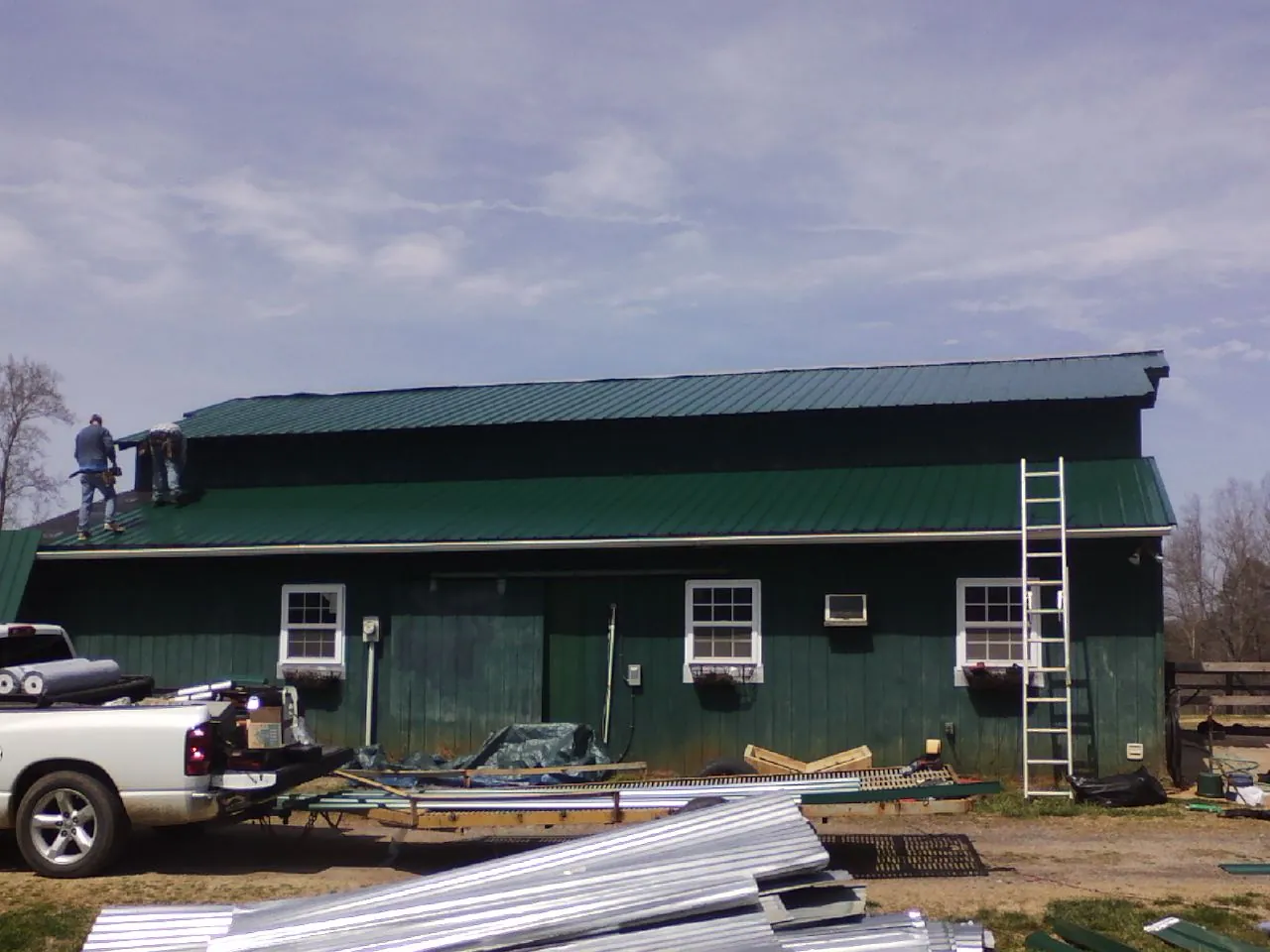 Crew installing green metal roofing on a large green barn in Sterling Heights