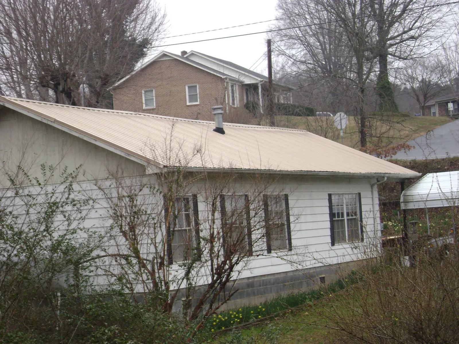 Tan metal roof on a white sided house set into a hillside — Commercial Roofing by Roofing Brothers in Sterling Heights