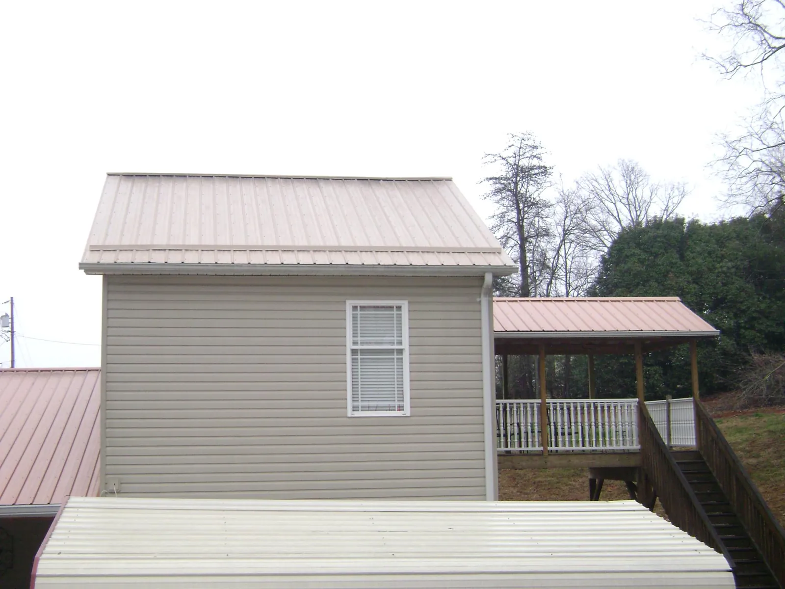 Tan metal roofs on a two story addition and attached porch, from a Roof Replacement job in Sterling Heights