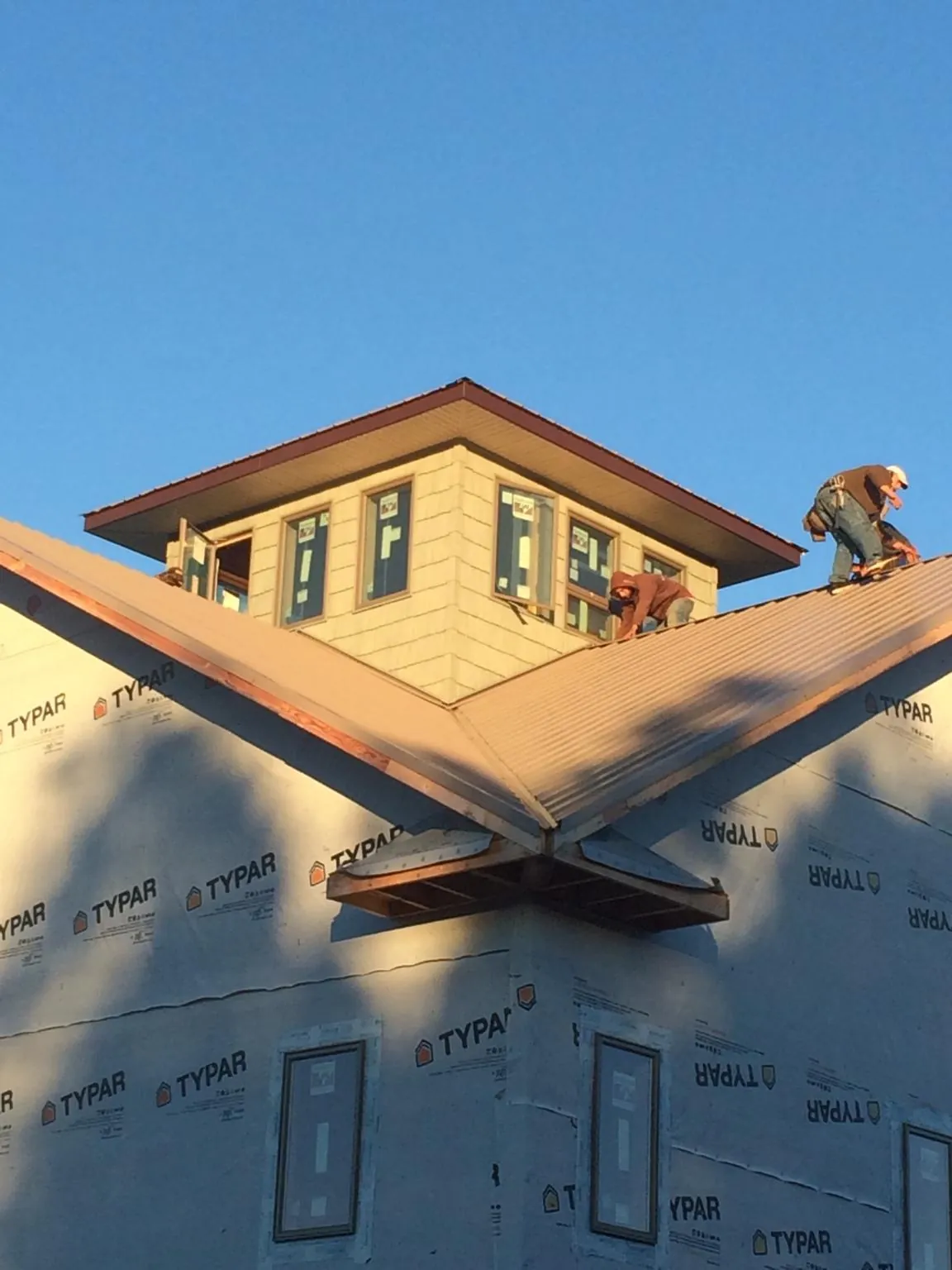 Roofers working around a rooftop cupola on a new metal roof at sunset — Roof Waterproofing in Sterling Heights by Roofing Brothers